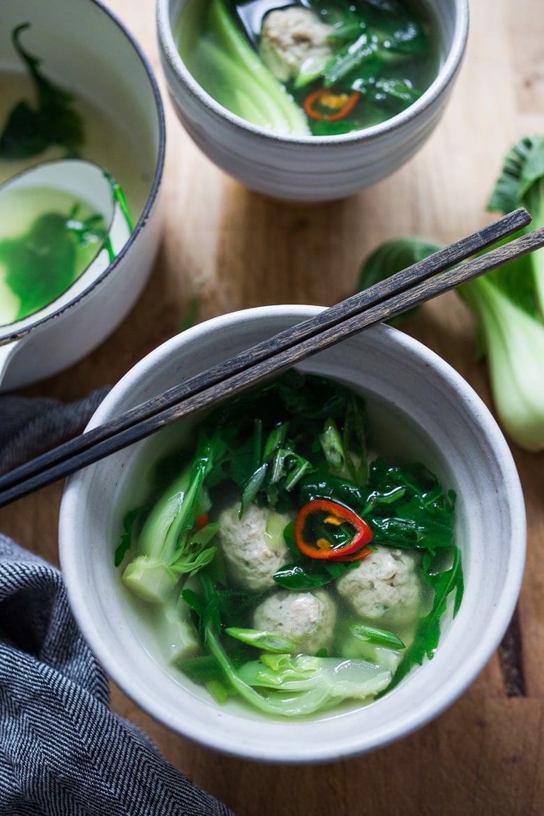 brothy chicken soup in bowl with dark greens and garnished with red chili.