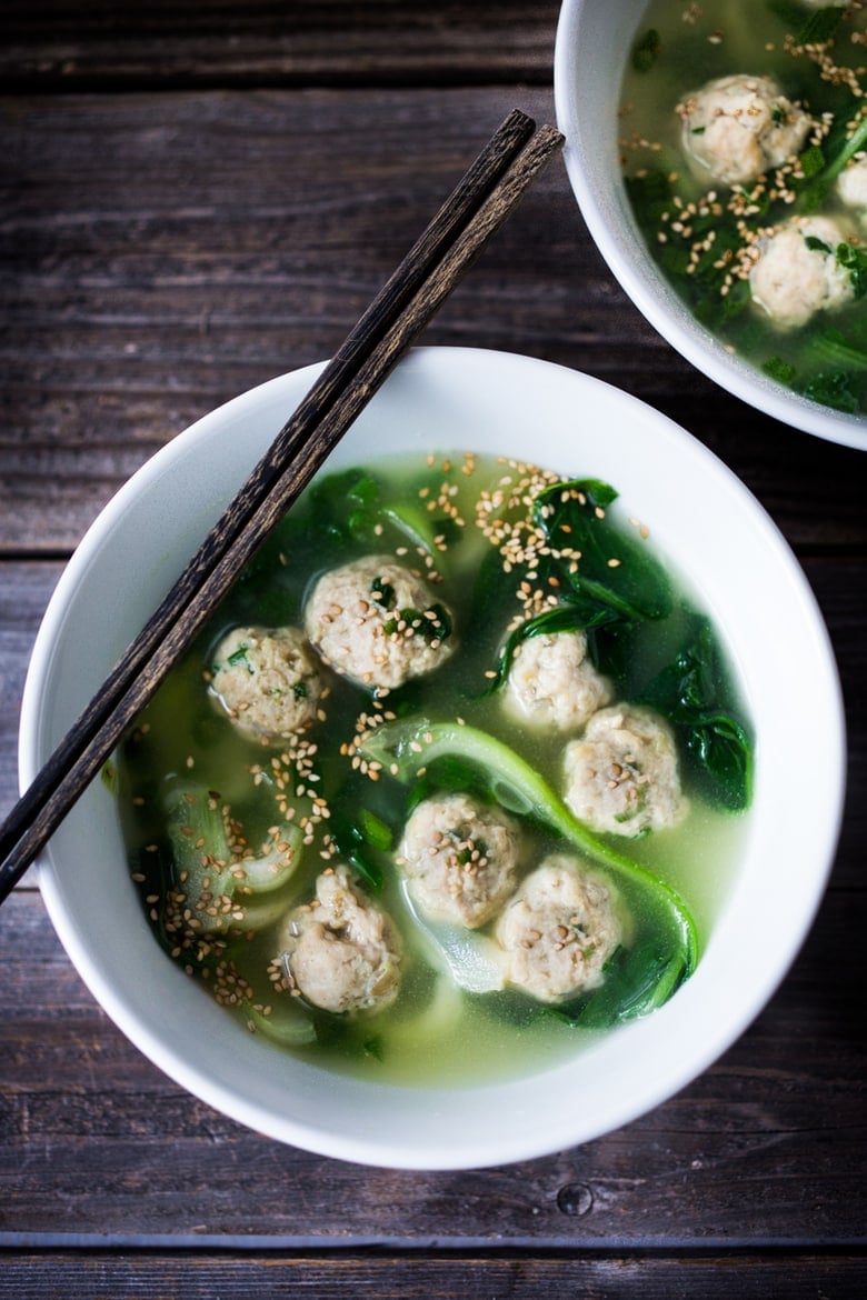 chicken meatball soup in bowl with dark greens, bok choy, and garnished with sesame seeds.