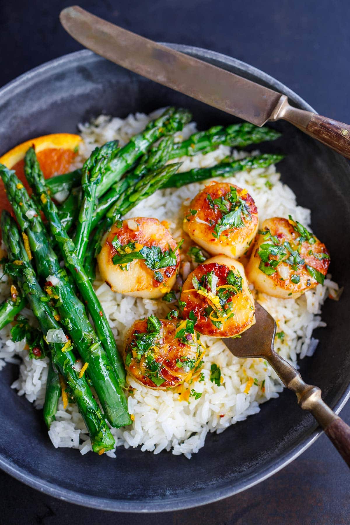 seared scallops in citrus dressing served over rice with asparagus and orange slice.