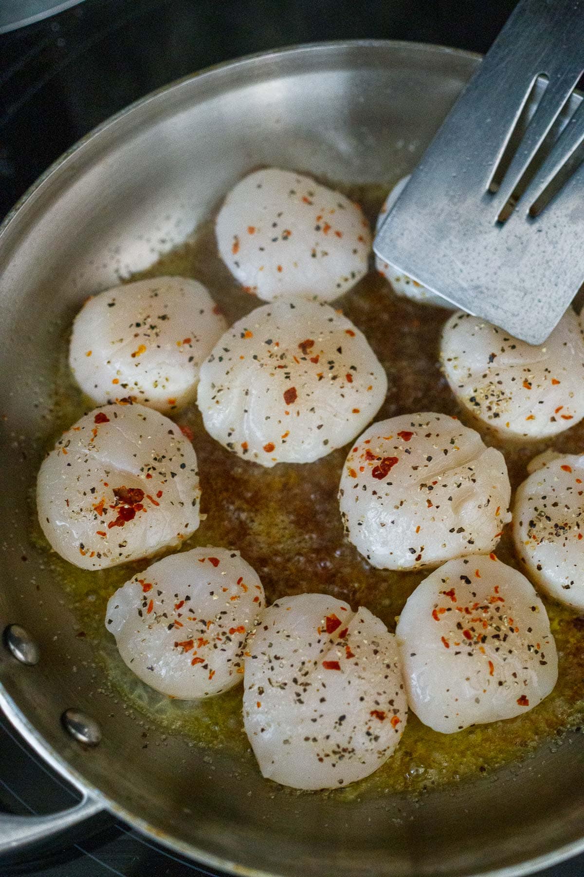 scallops cooking in skillet with seasoning.