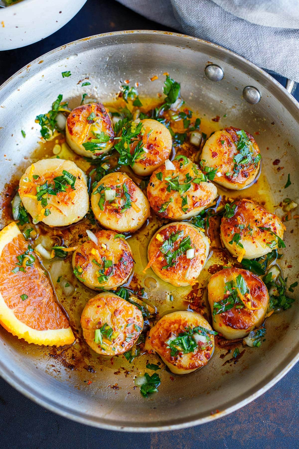 seared scallops with herby citrus dressing in skillet with orange wedge.