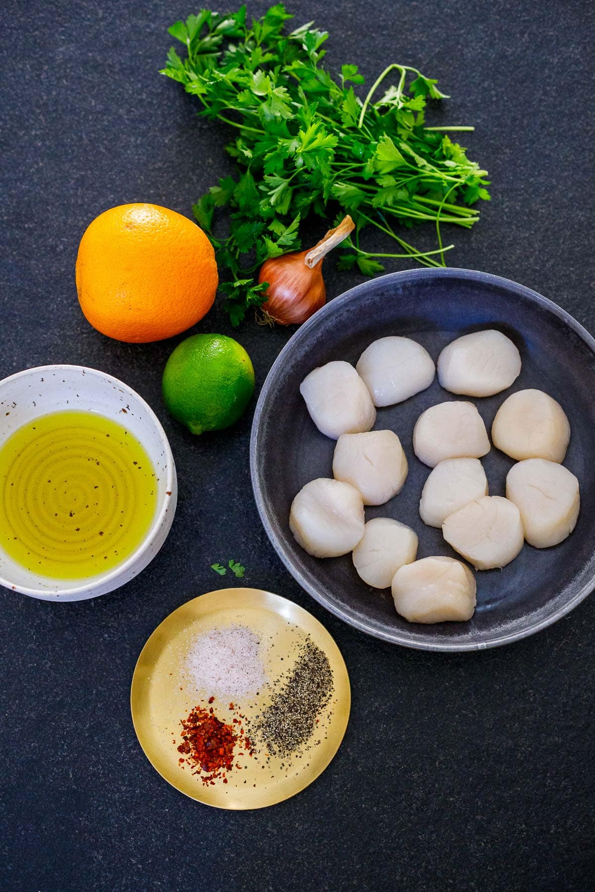 seared scallops ingredients laid out - dry scallops, shallot, herbs, orange, lime, oil, salt, pepper, chili flakes.