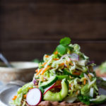 Introducing Tlayudas! Traditional Oaxacan street food, tlayudas are a cross between a tostada and a pizza, made with a crispy tortilla, topped with refried beans, cheese (optional) cabbage slaw, avocado and cilantro. This healthy version is vegan and GF adaptable! | #tlayudas #tostadas #mexicanpizza #vegan #oaxacanfood #mexicanstreetfood #veganmexican #healthymexicanrecipes | www.feastingathome.com