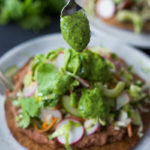 Introducing Tlayudas! Traditional Oaxacan street food, tlayudas are a cross between a tostada and a pizza, made with a crispy tortilla, topped with refried beans, cheese (optional) cabbage slaw, avocado and cilantro. This healthy version is vegan and GF adaptable! | #tlayudas #tostadas #mexicanpizza #vegan #oaxacanfood #mexicanstreetfood #veganmexican #healthymexicanrecipes | www.feastingathome.com