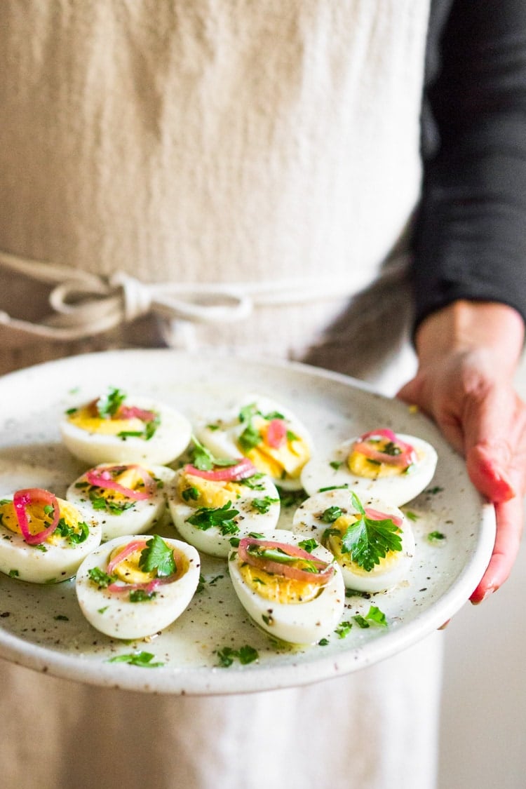 Quick and Easy Hard boiled eggs with olive oil, fresh herbs and pickled shallots, a simple, make ahead brunch recipe that is  perfect for gatherings and potlucks. Think of these like deviled eggs but in ½ the time! #deviledeggs #hardboiledeggs #boiledeggs #brunchrecipe 