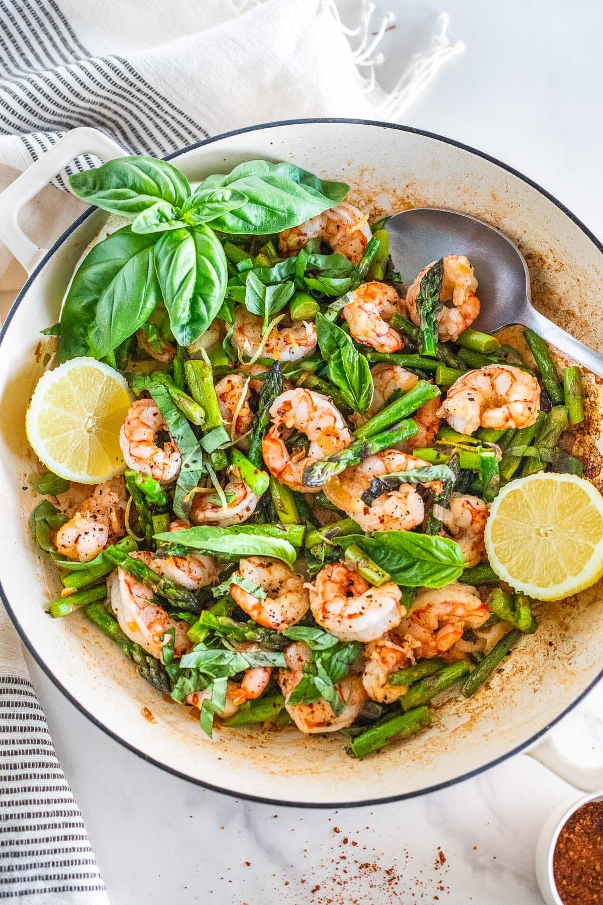 Dutch oven with one pan shrimp and asparagus with basil, lemon halves, and a spoon. 