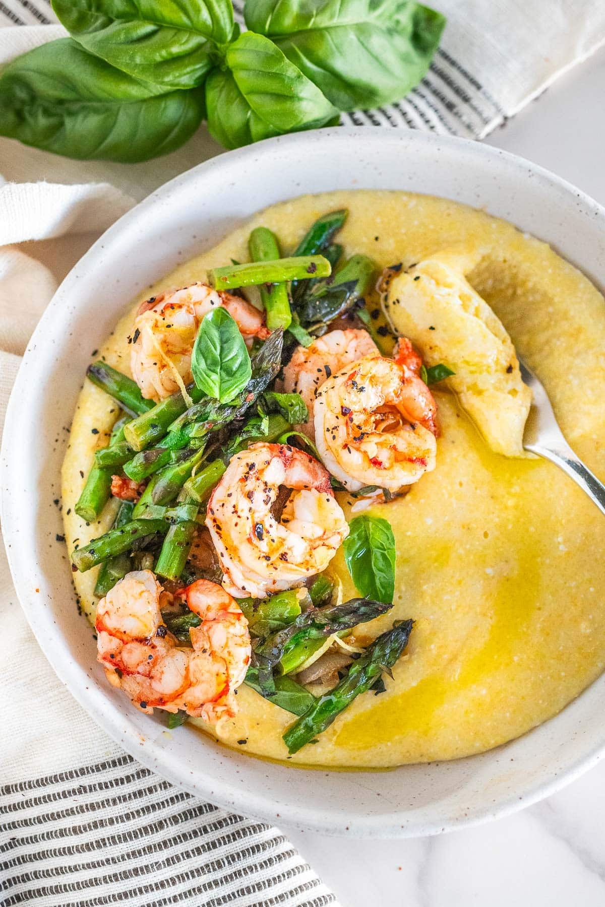 bowl of polenta with one pan shrimp and asparagus on top with fresh basil.