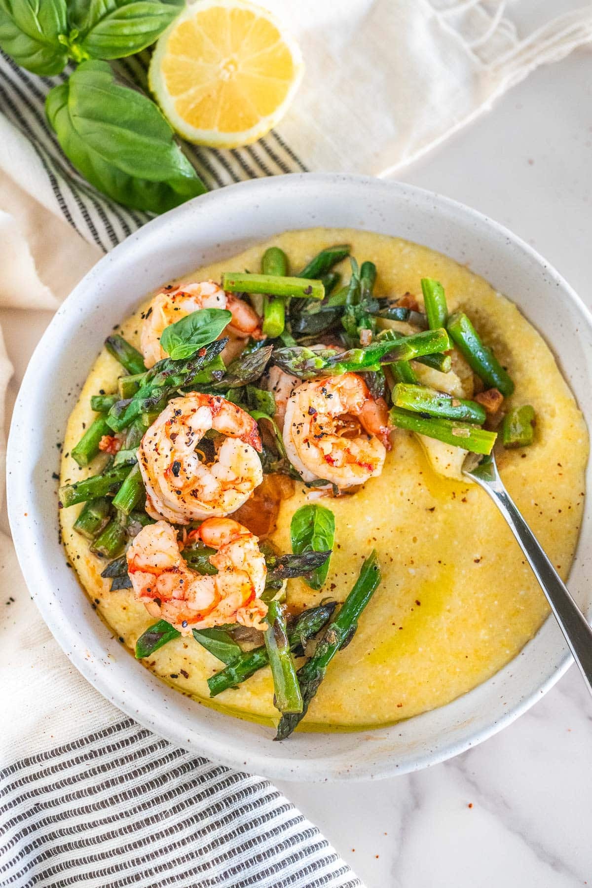 one pan shrimp and asparagus with basil on top of polenta in a bowl.