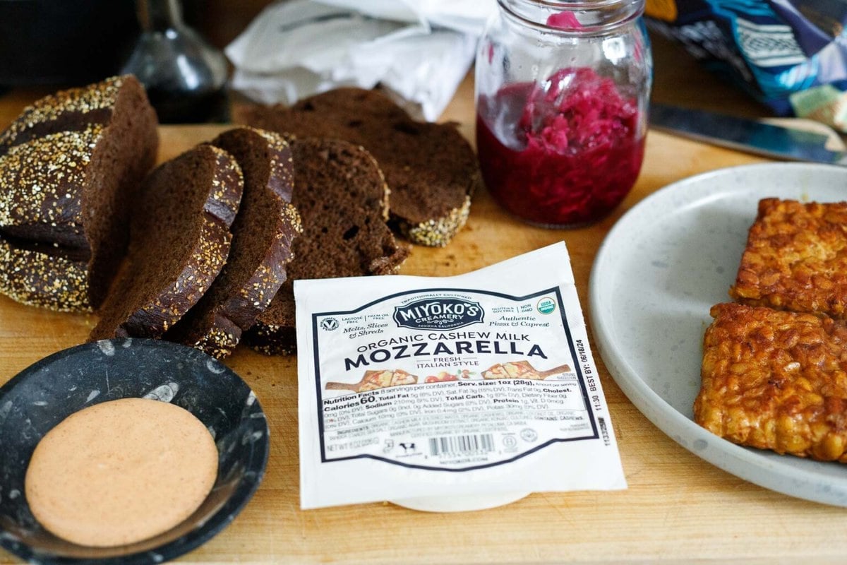 tempeh reuben sandwich ingredients on a wood block, using vegan cheese.