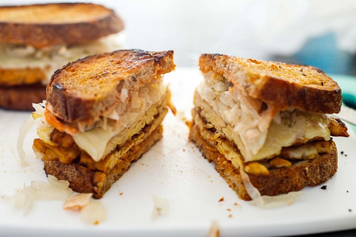 cutting the tempeh reuben sandwich in half on a cutting board,