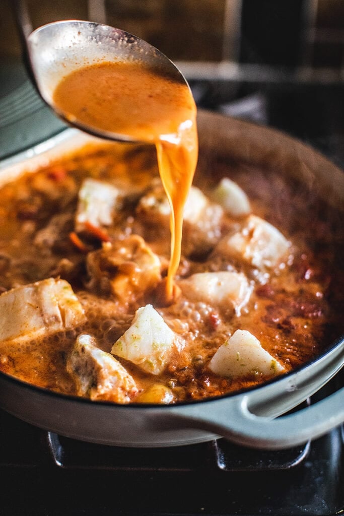 ladle spooning Moqueca broth over the fish fillets. 