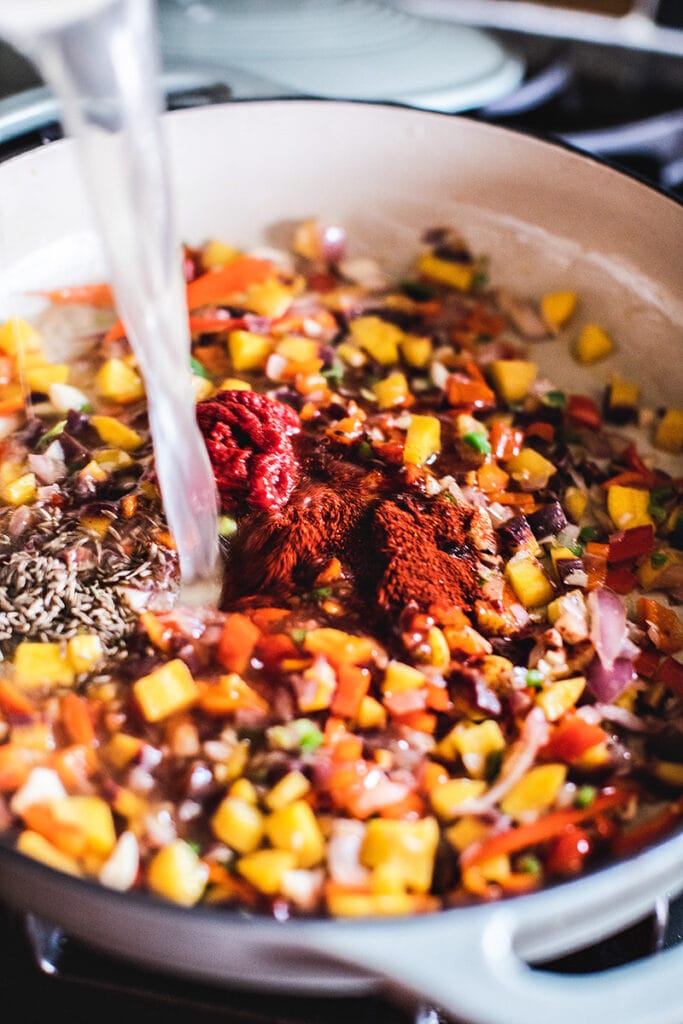 pouring stock into pan of sautéed vegetables with spices and tomato paste.