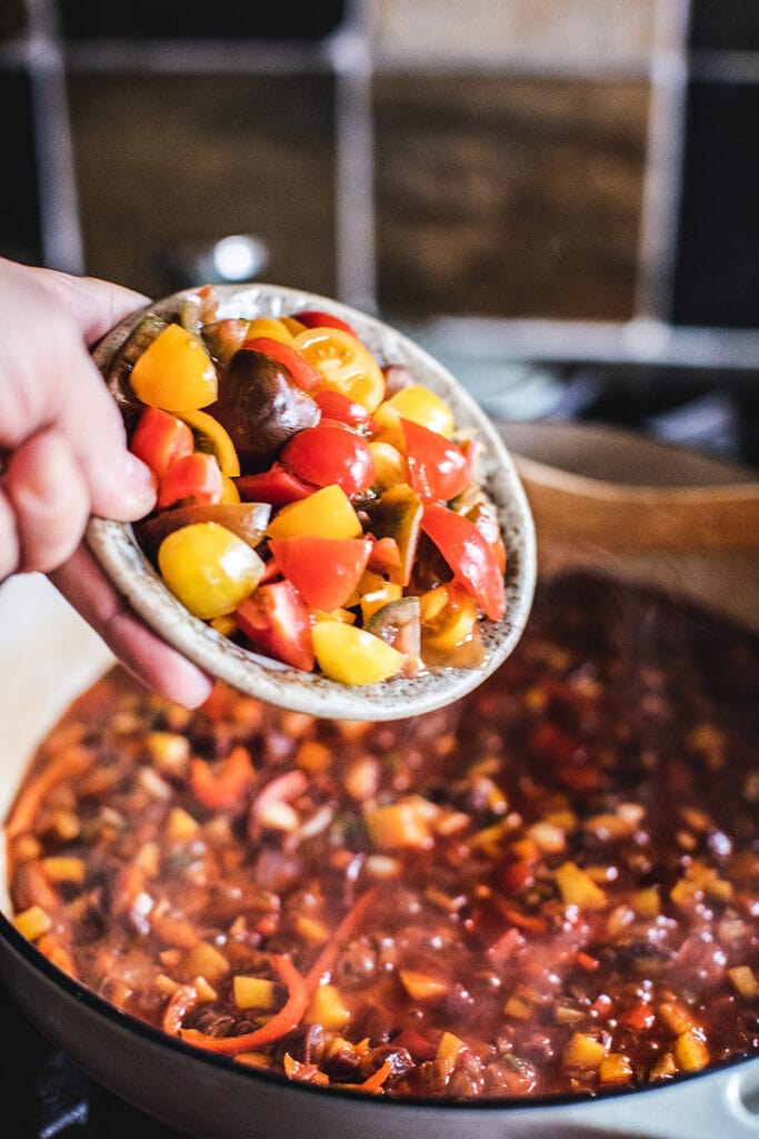 pouring bowl of quartered cherry tomatoes into Moqueca, a Brazilian stew.