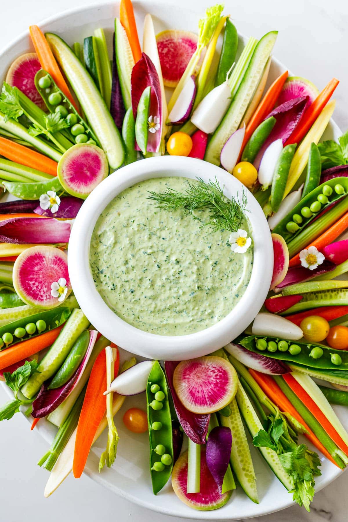 A crudité platter with green goddess dressing on a white counter.