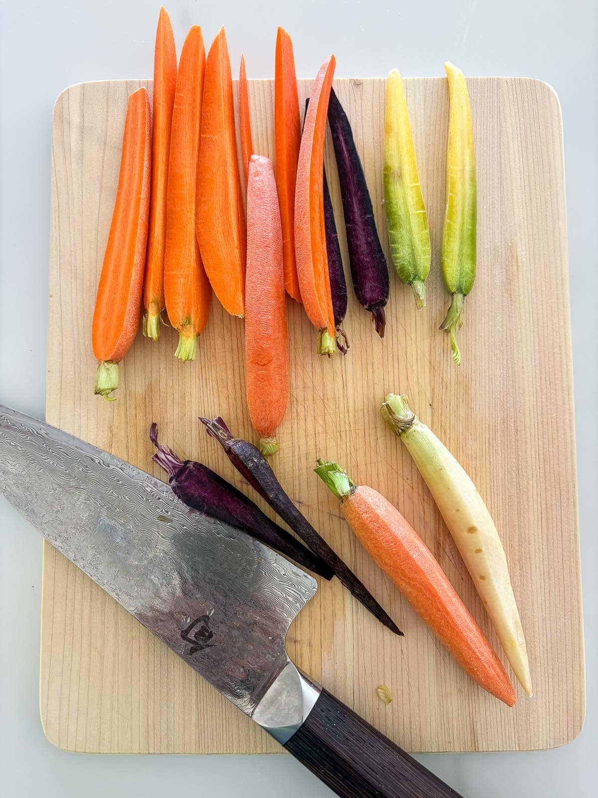 wood board and sharp knife slicing rainbow carrots into strips.