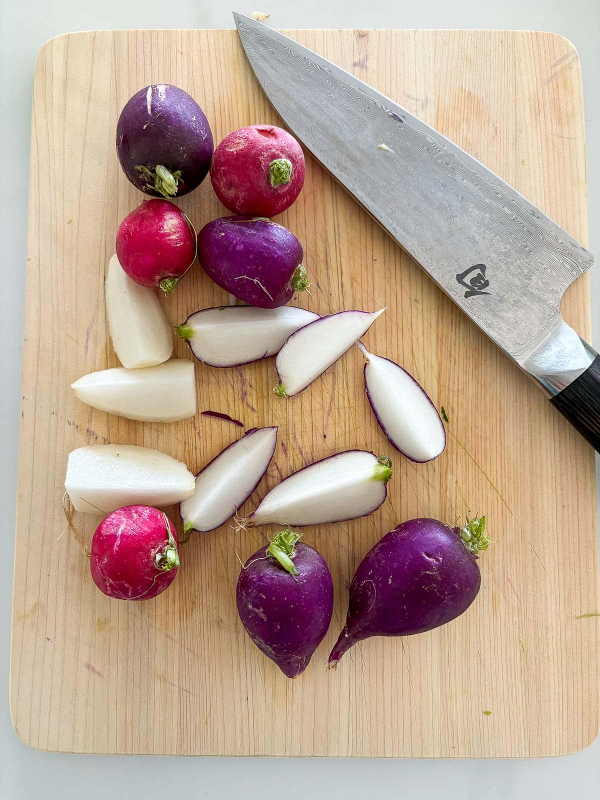 wood board and sharp knife with purple and red radishes cut into wedges.