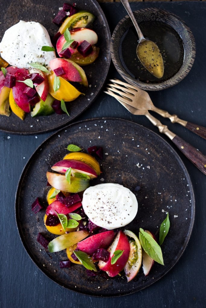 plate of tomato nectarine salad arranged around burrata with forks.