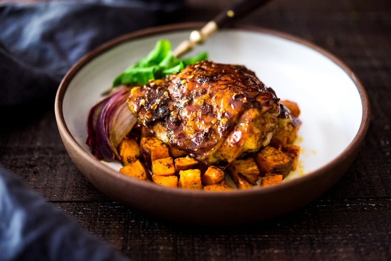 harissa chicken on bed of roasted sweet potatoes with red onion wedge.