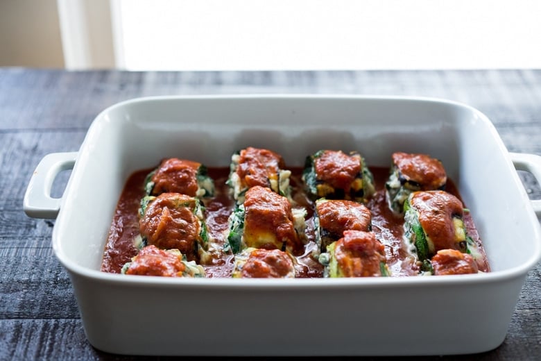 baking dish with assembled zucchini lasagna roll ups topped with marinara.