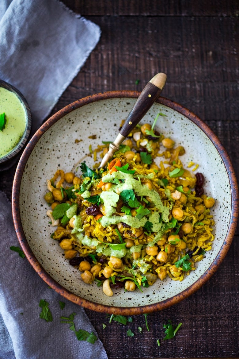 a bowl of vegetable biryani topped with mint-yogurt chutney.