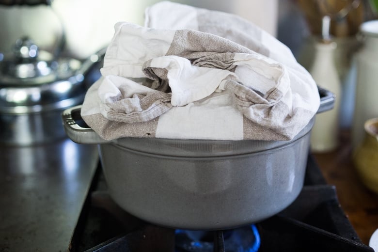 A pot on the stove with a towel tucked under and around the lid.