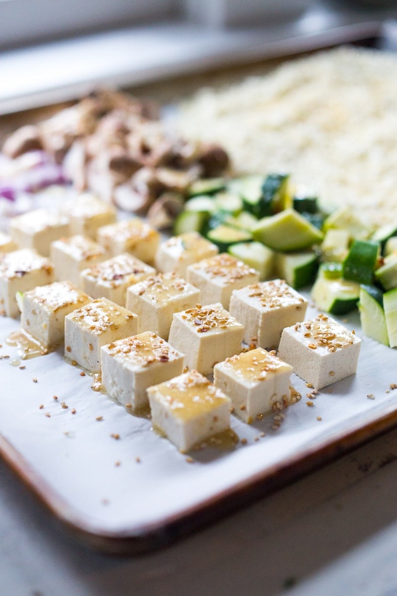 close up of cubed tofu with marinade over top with sesame seeds and zucchini in background.