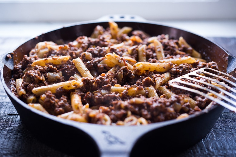 penne stirred into cast iron skillet with lamb bolognese sauce.