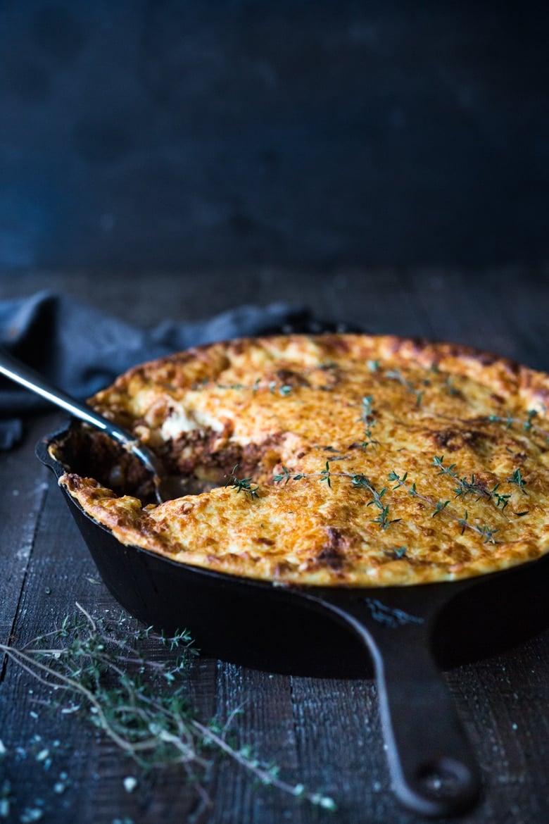 baked Greek pasta with lamb (pastitsio) in a cast iron skillet with cheesy bechamel sauce topping and fresh thyme.