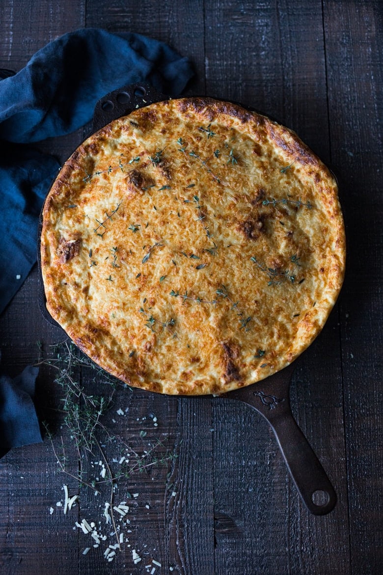 baked Greek pasta with lamb in cast iron skillet- pastitsio with a cheesy béchamel layer, golden and crispy, garnished with fresh thyme.