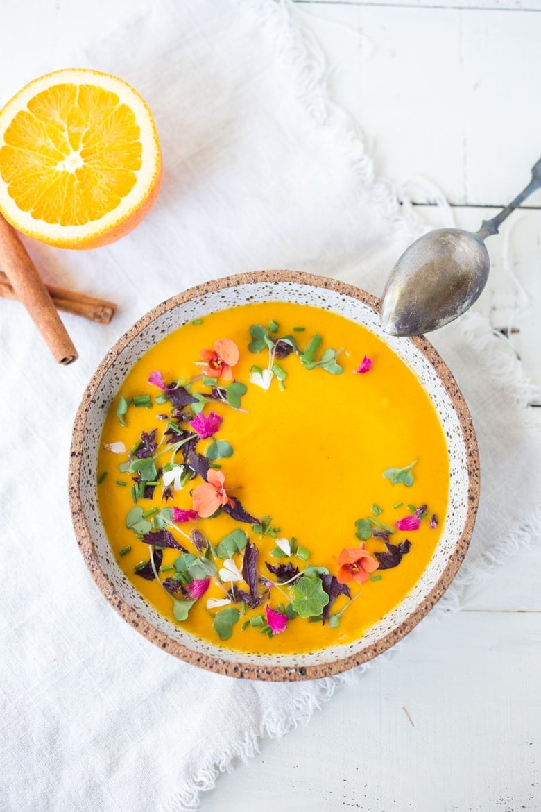 creamy Moroccan carrot soup in bowl, garnished with edible flowers and microgreens.