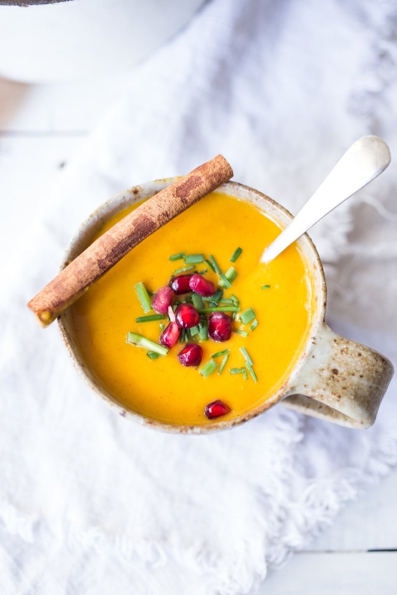 Moroccan carrot soup in mug with pomegranate seeds and chives, served with cinnamon stick.