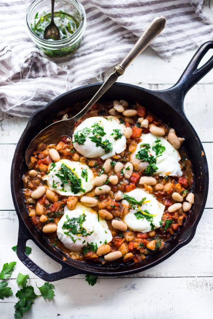 Tuscan farmers breakfast with cannellini bean stew topped with poached eggs and gremolata in cast iron skillet.