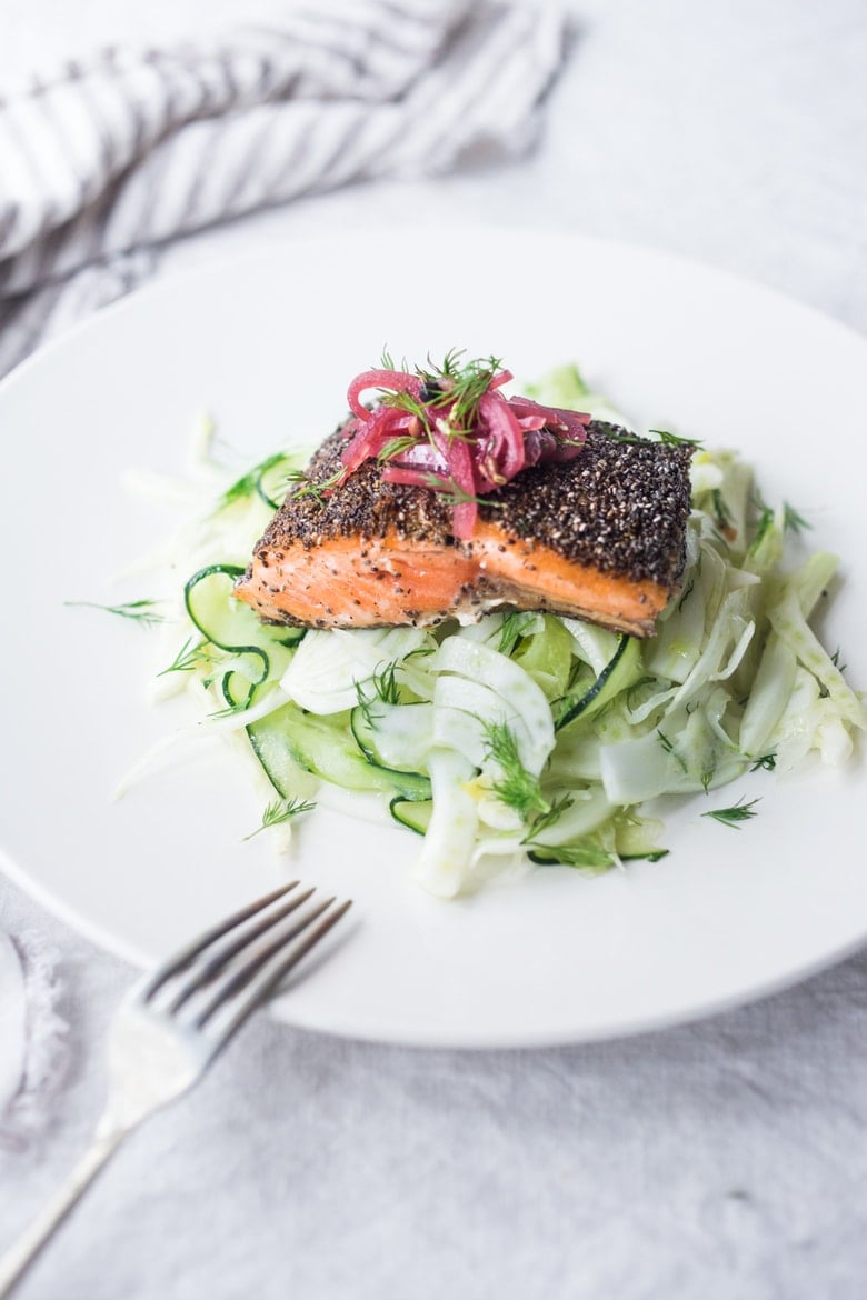 pan-seared salmon with chia seed crust served over fennel salad, garnished with pickled red onions and fresh dill.