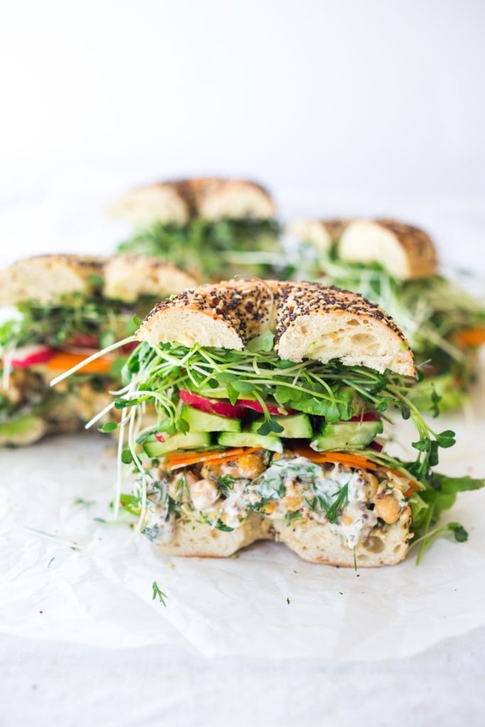 chickpea salad sandwich on everything bagel with microgreens, sliced cucumber, sliced avocado, and sliced carrots.