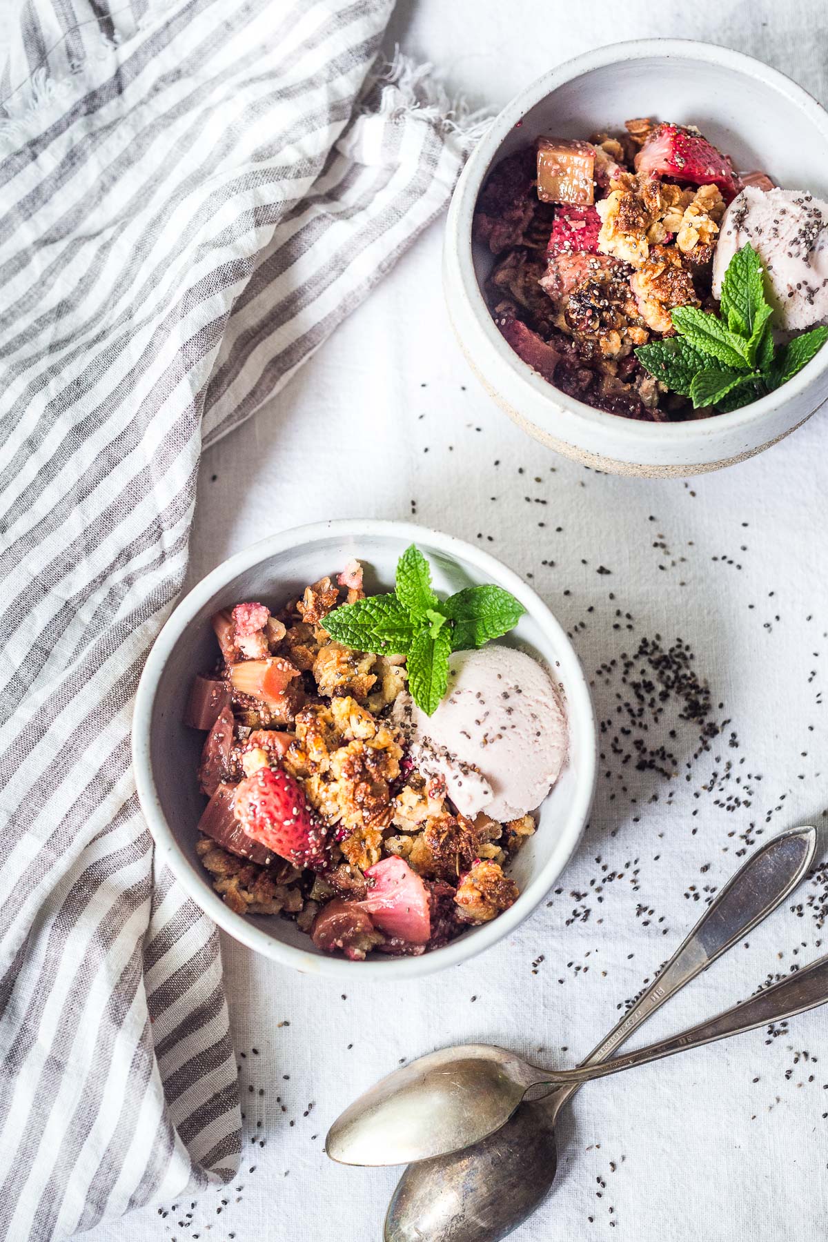 bowl of strawberry rhubarb crisp with oat crumble topping served with scoop of strawberry ice cream and fresh mint garnish.