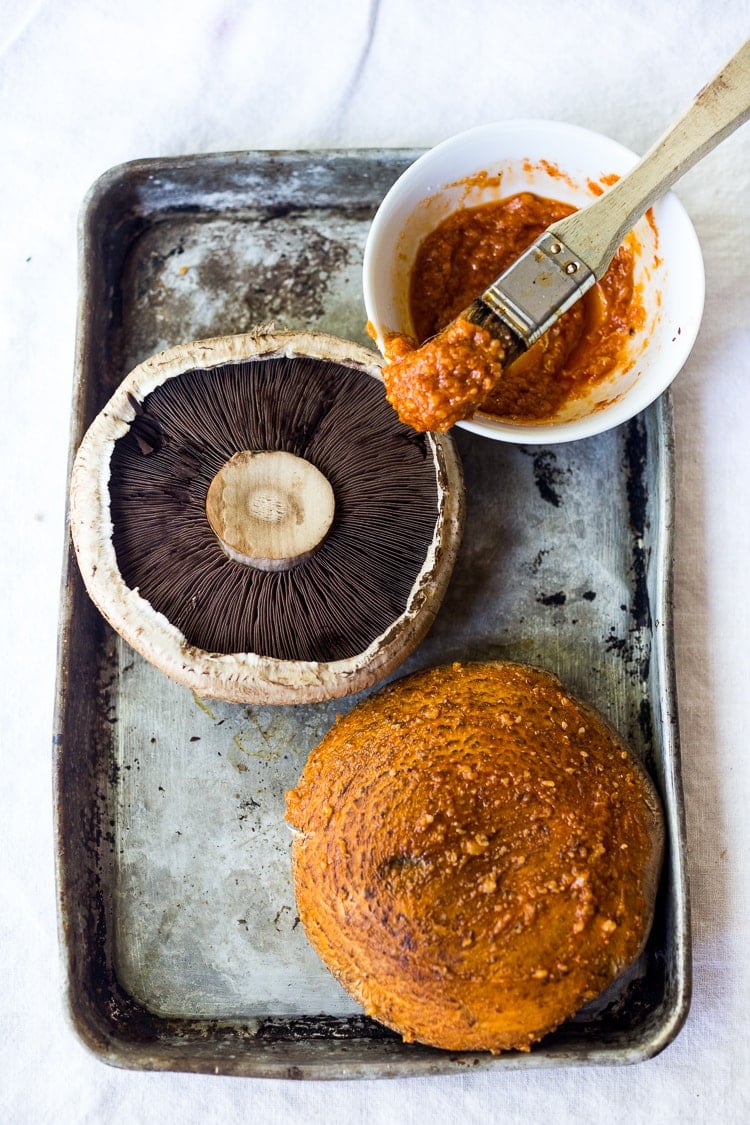 portobello mushrooms on baking sheet with small bowl of miso-sesame-sriracha marinade and brush.