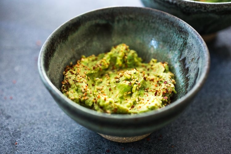 small bowl with Asian guacamole, topped with sesame seeds and chili flakes.