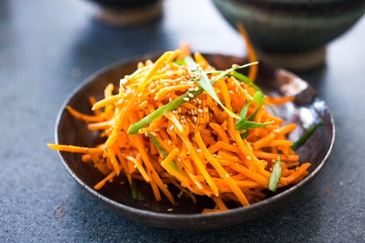 small dish with carrot slaw, garnished with scallion ribbons and toasted sesame seeds.