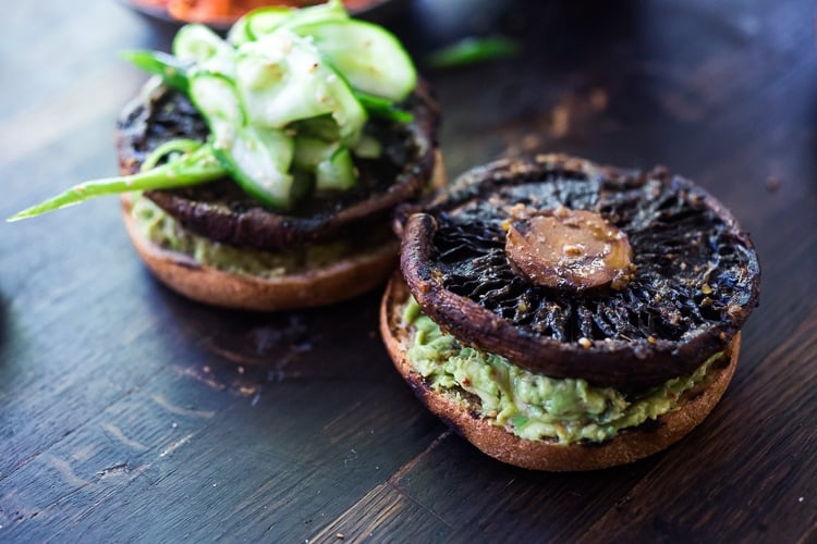 assembling portobello mushroom burgers- Asian guacamole on grilled buns with grilled portobello on top, garnished with cucumber ribbon salad.