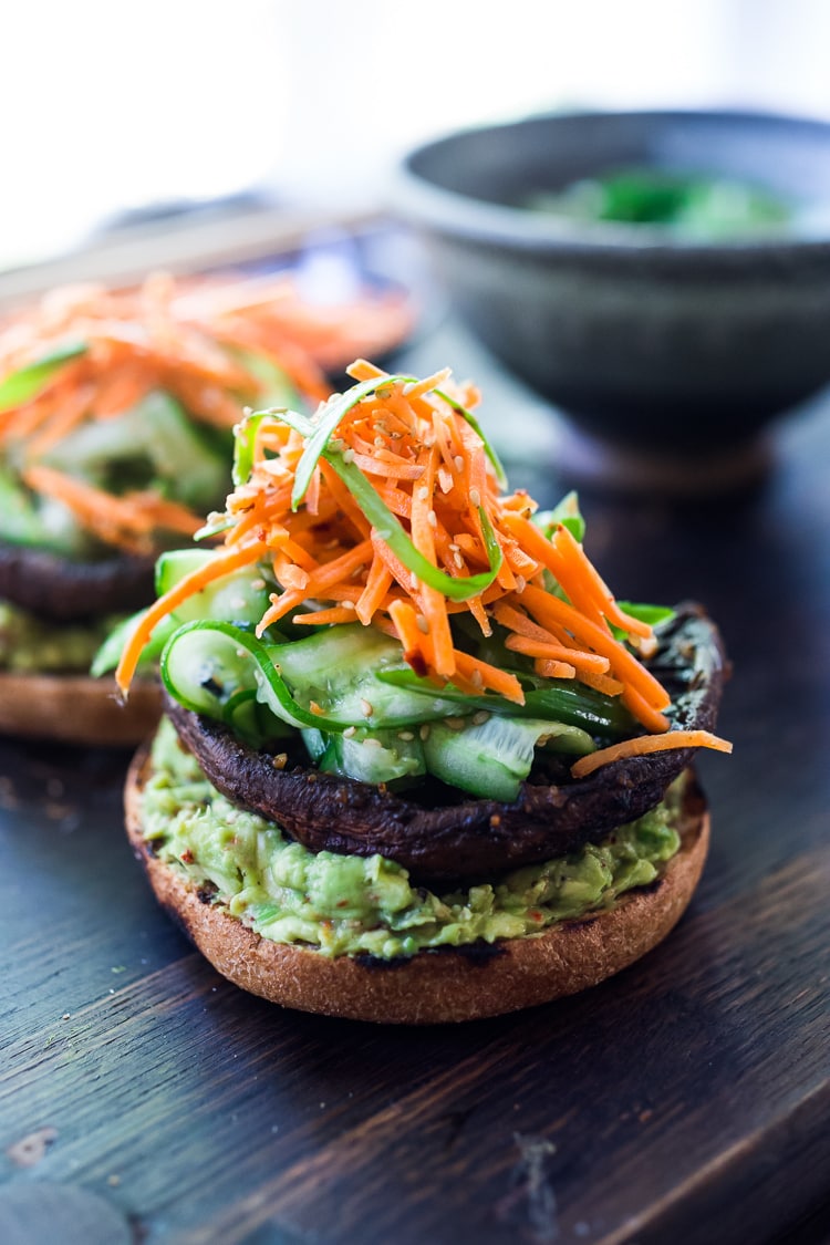 This Asian-style, grilled, vegan portobello mushroom burger is full of delicious umami flavor! It's lathered with Asian-style Guacamole, topped with a cool cucumber ribbon salad and crunchy carrot slaw. Healthy, delicious and really satisfying. AND totally vegan! #veganburger #portobelloburger #veganportobelloburger #portobellomushroomrecipes #portobello #vegan #veganburger #grilled #grilledportobello 