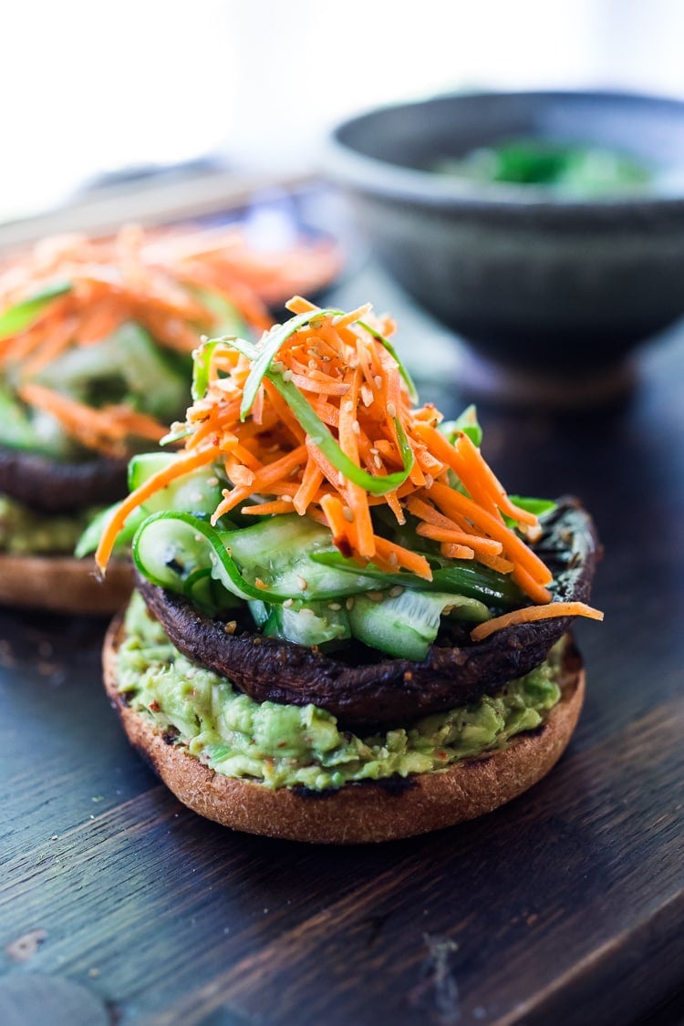 open-faced portobello mushroom burgers topped with Asian guacamole, grilled portobello, cucumber ribbon salad, carrot slaw, sesame seeds, and scallion.