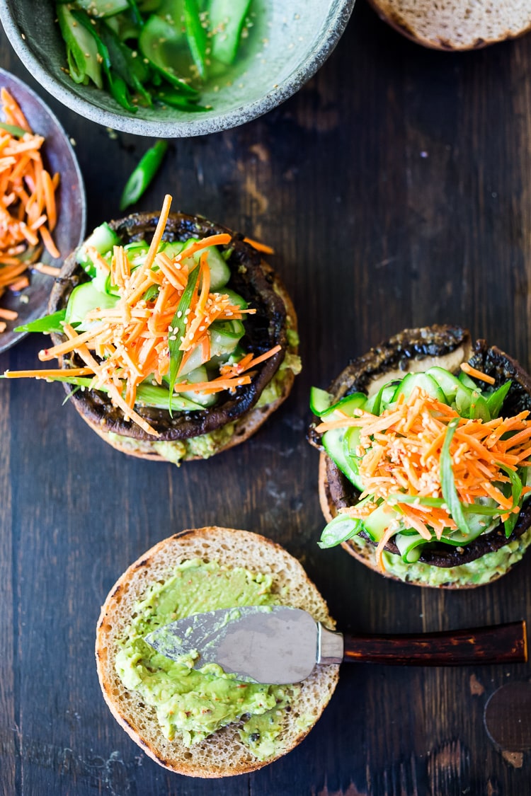 This Asian-style, grilled, vegan portobello mushroom burger is full of delicious umami flavor! It's lathered with Asian-style Guacamole, topped with a cool cucumber ribbon salad and crunchy carrot slaw. Healthy, delicious and really satisfying. AND totally vegan! #veganburger #portobelloburger #veganportobelloburger #portobellomushroomrecipes #portobello #vegan #veganburger #grilled #grilledportobello 