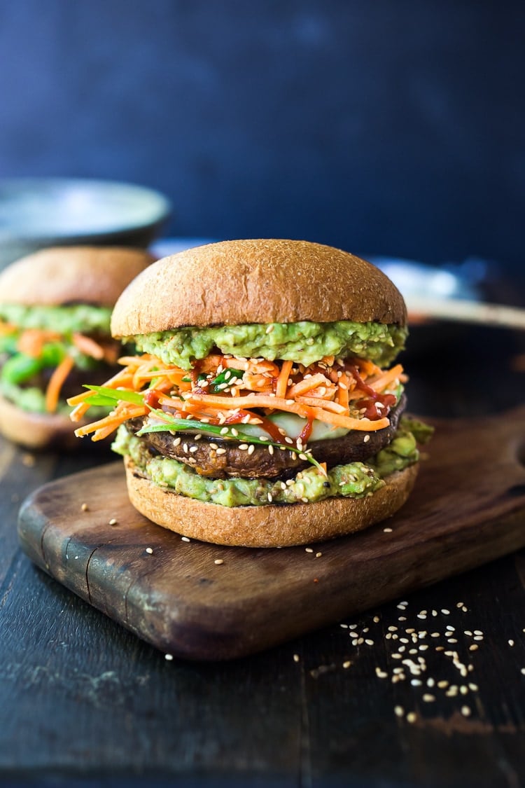 portobello mushroom burger with Asian guacamole, cucumber salad, carrot slaw, and sriracha in between wheat buns.