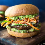 This Asian-style, grilled, vegan portobello mushroom burger is full of delicious umami flavor! It's lathered with Asian-style Guacamole, topped with a cool cucumber ribbon salad and crunchy carrot slaw. Healthy, delicious and really satisfying. AND totally vegan! #veganburger #portobelloburger #veganportobelloburger #portobellomushroomrecipes #portobello #vegan #veganburger #grilled #grilledportobello