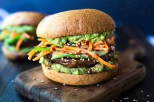 This Asian-style, grilled, vegan portobello mushroom burger is full of delicious umami flavor! It's lathered with Asian-style Guacamole, topped with a cool cucumber ribbon salad and crunchy carrot slaw. Healthy, delicious and really satisfying. AND totally vegan! #veganburger #portobelloburger #veganportobelloburger #portobellomushroomrecipes #portobello #vegan #veganburger #grilled #grilledportobello