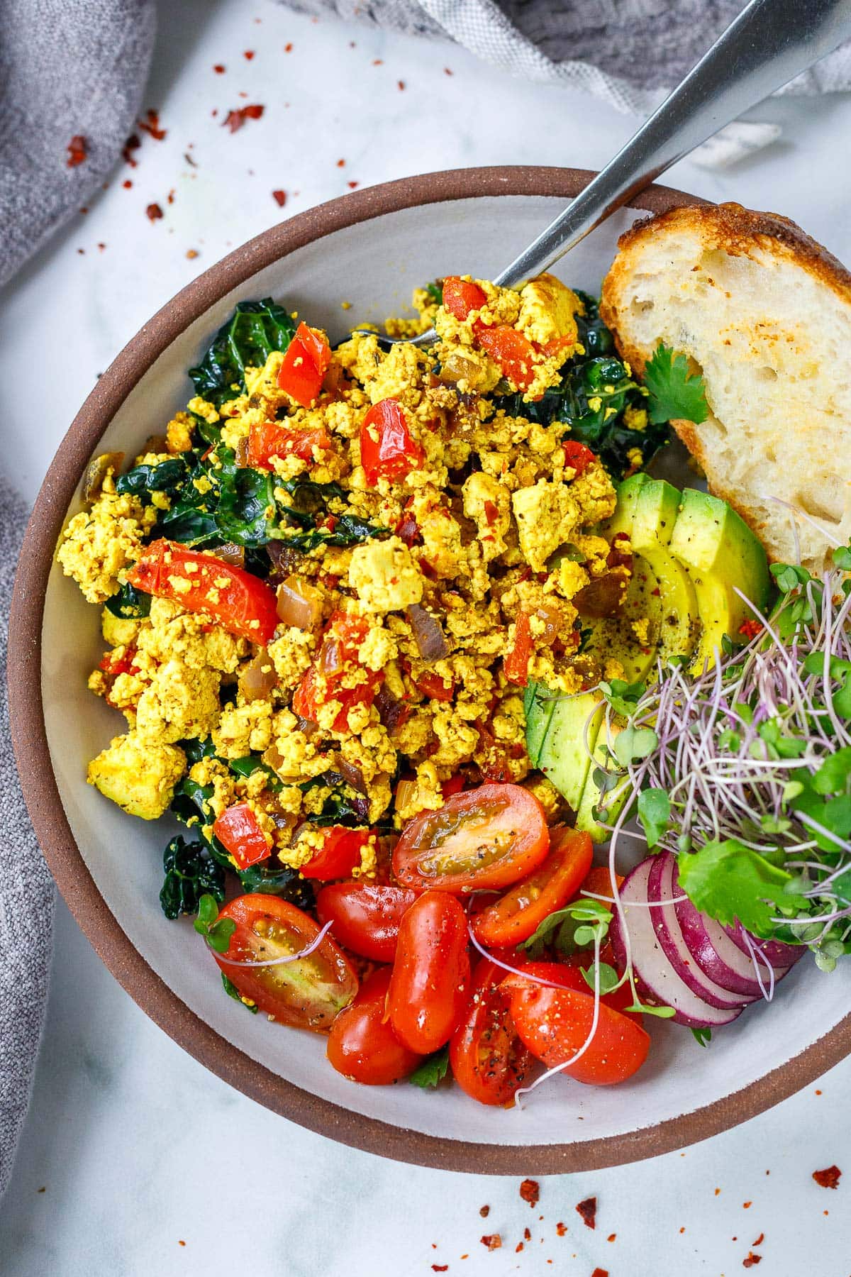 Tofu scrambe served in a bowl with avocado, sprouts, tomatoes and toast. 