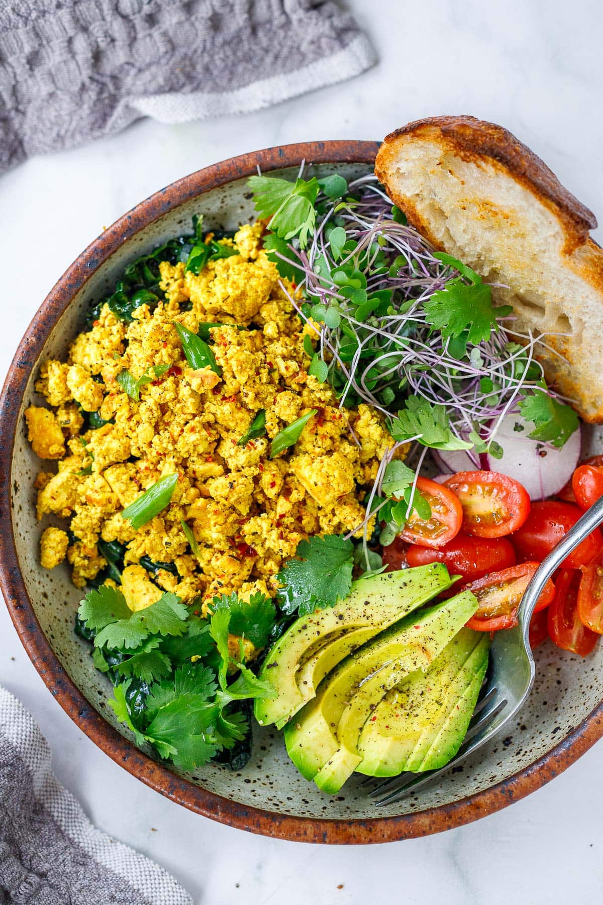 Tofu scramble served in a bowl with avocado, sprout, tomatoes and toast. 