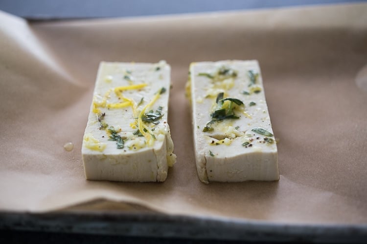 tofu in lemon tarragon marinade on parchment-lined baking sheet.