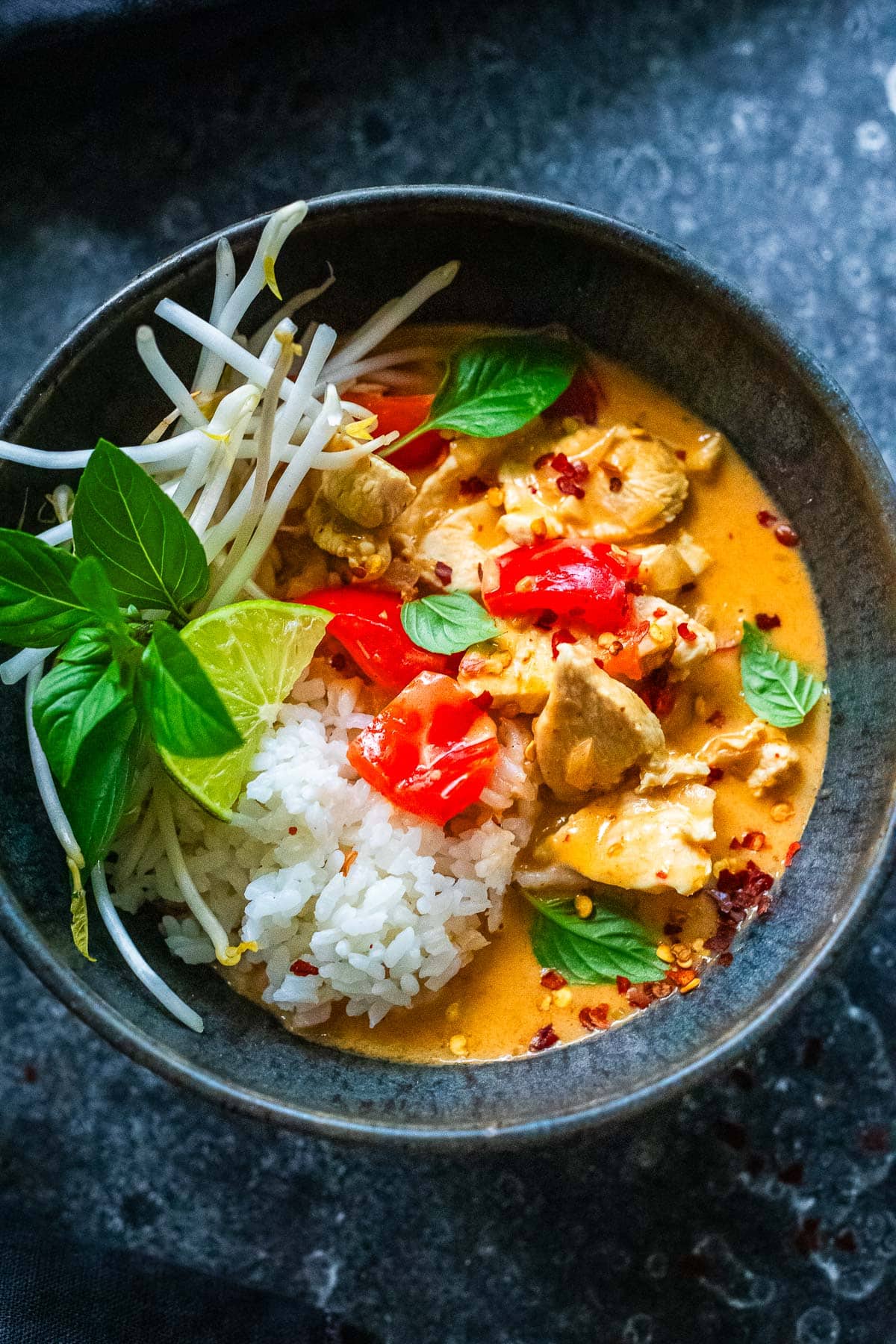 Thai red curry in a bowl with jasmine rice, bean sprouts, lime and Thai Basil. 