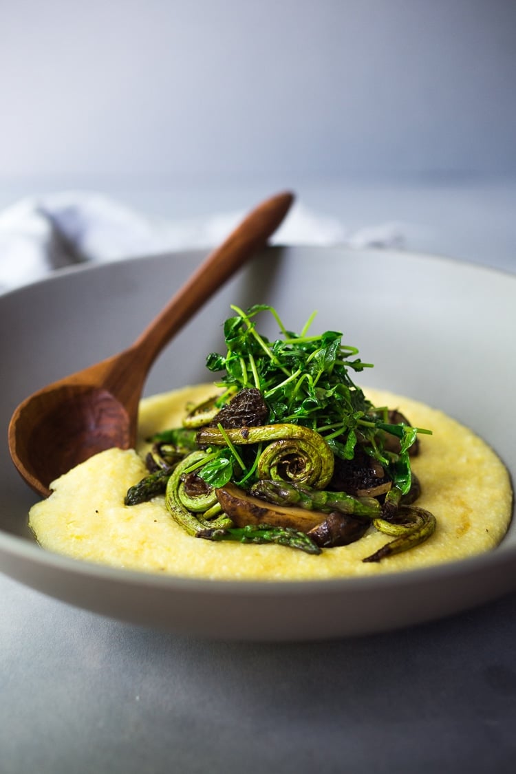 bowl of creamy polenta topped with spring veggies and pea shoots.